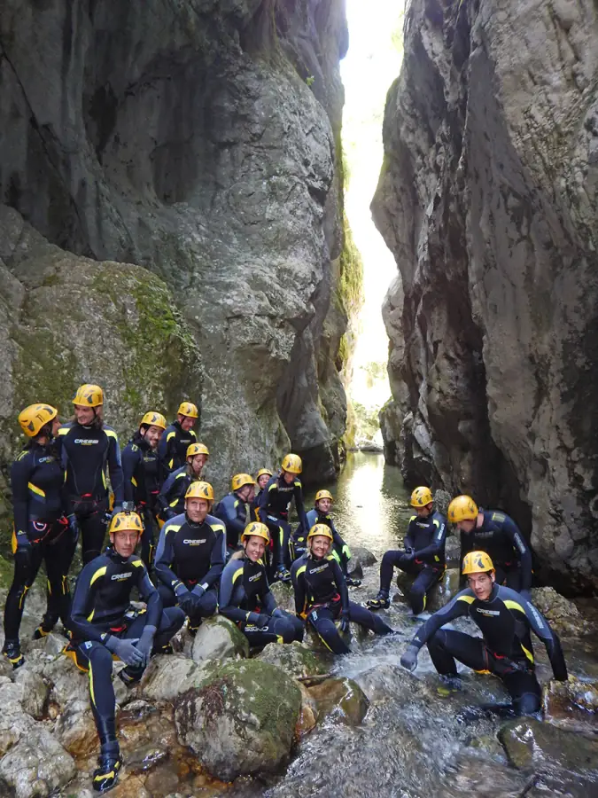 A group of canyoners in wetsuits and yellow helmets in a narrow limestone canyon