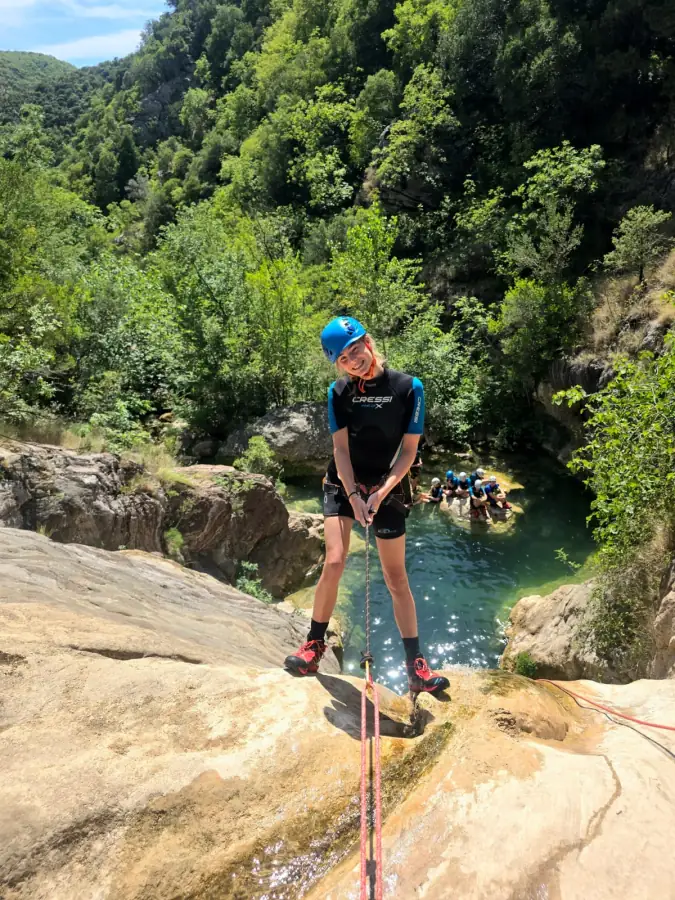 A canyoner starting a rappel above a deep green pool