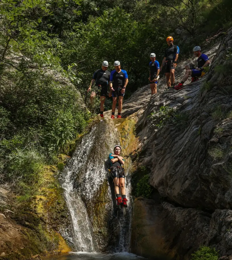 A canyoner descending a waterfall while the group watches from the rock above