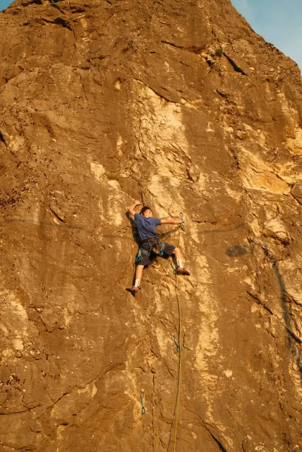 A lead climber high on a golden limestone wall in evening light