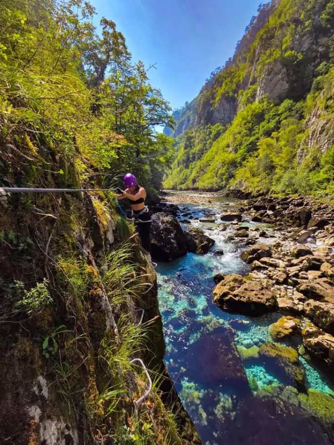 A via ferrata traverse on a steel cable above a turquoise river canyon
