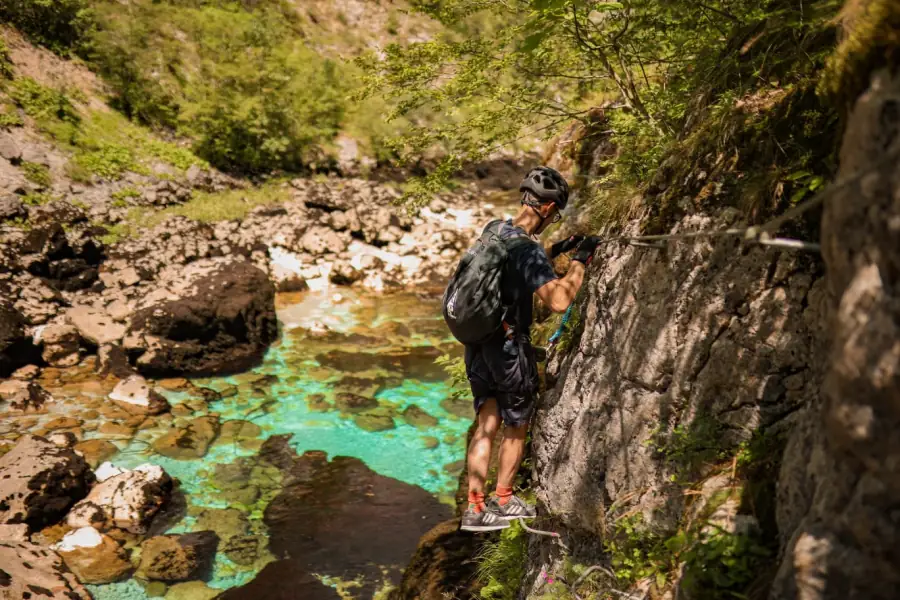 A climber on a via ferrata cable above brilliant turquoise water